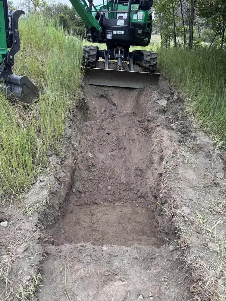 Compact excavator carefully exposing a buried system area