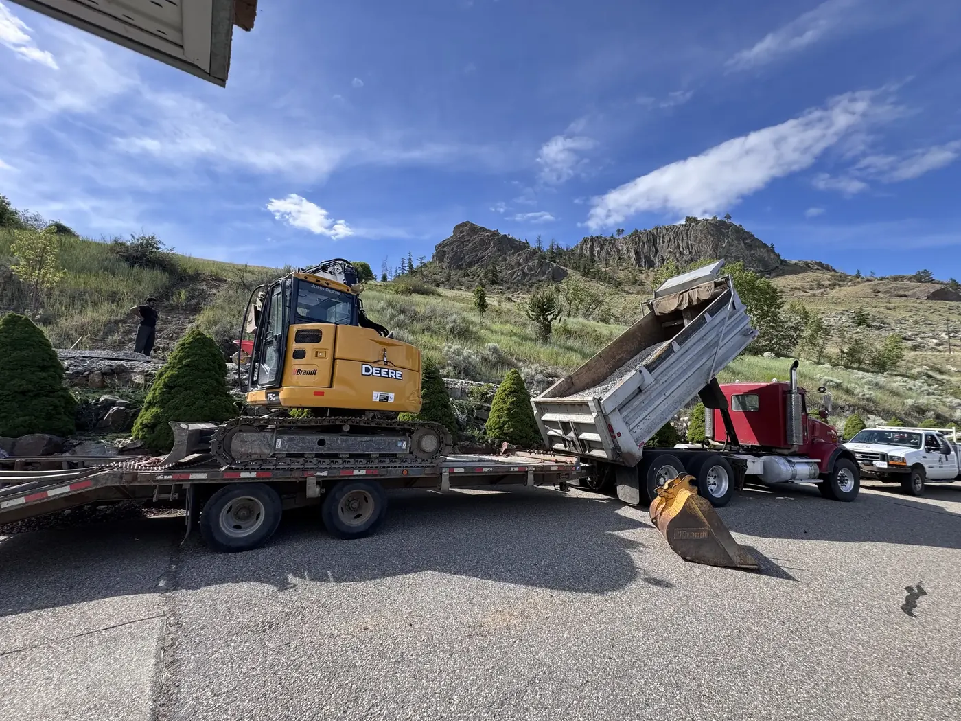 Excavator loading aggregate from a dump truck on a steep Shuswap property