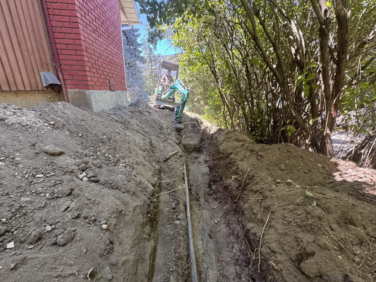 Compact excavator trenching beside a building for new line work